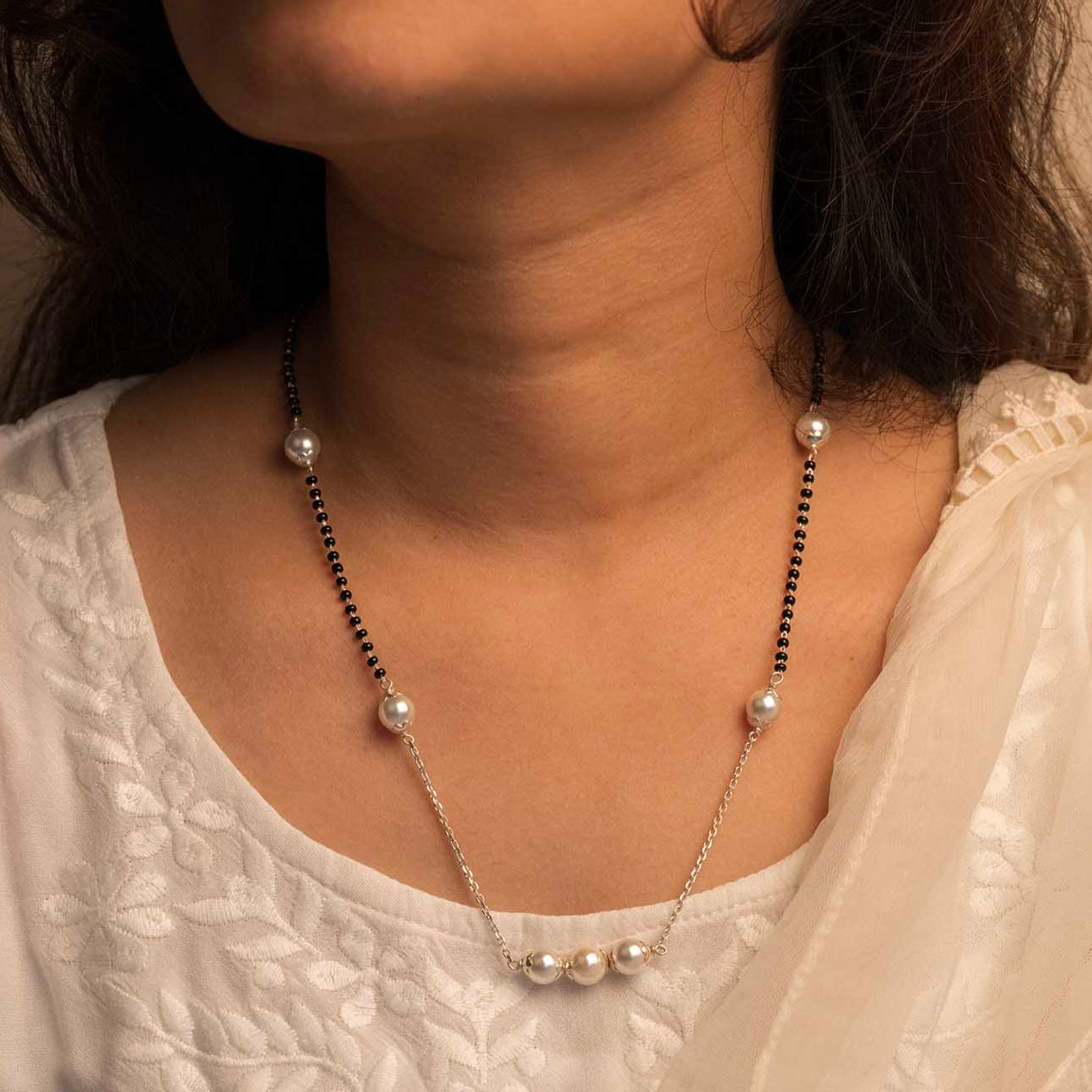 Close-up of a person wearing a pearl necklace with a neutral background