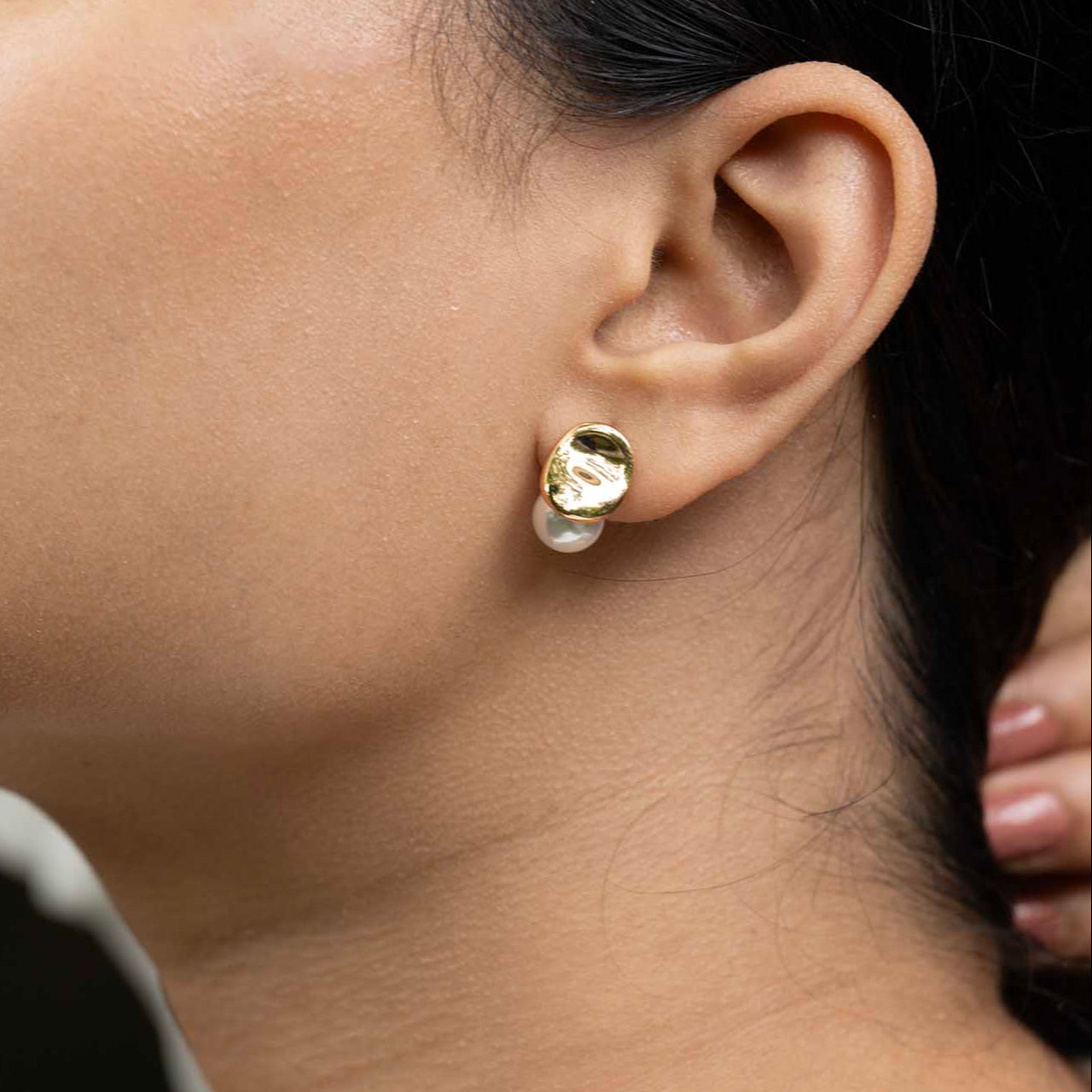 Close-up of an ear wearing a gold earring with a pearl center.