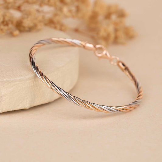 Two-tone gold and silver bracelet on a beige surface with dried flowers in the background