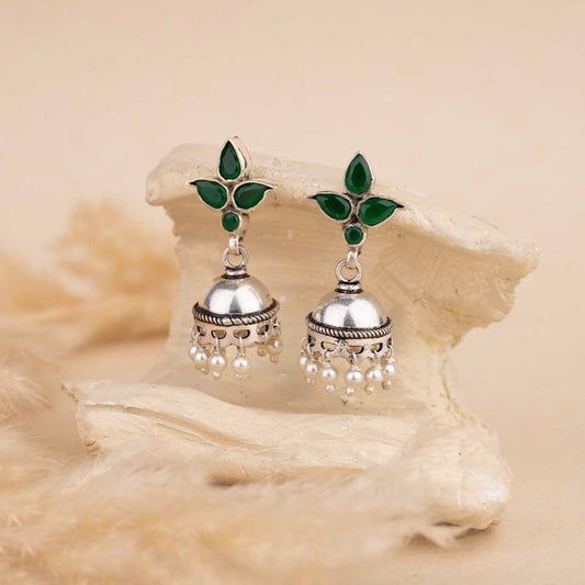 Silver earrings with green leaves on a beige shell background