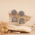Pair of silver earrings on a textured beige surface with dried flowers.
Silver Jhumka
