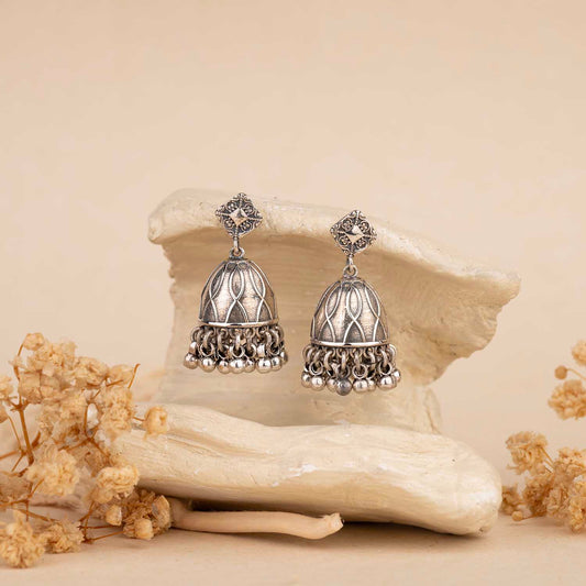 Pair of silver earrings on a decorative stone with dried flowers around jhumka
