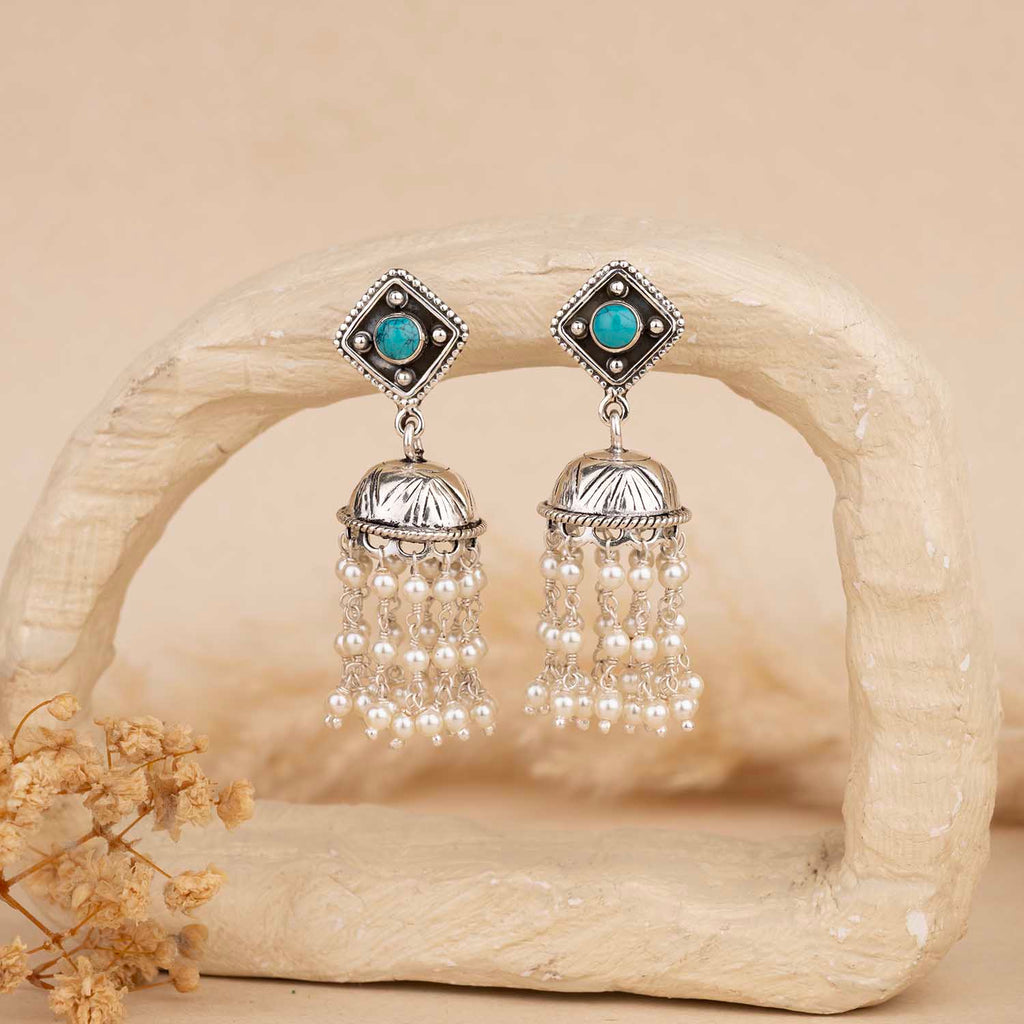 Pair of silver earrings with turquoise stones and pearl-like beads on a beige background