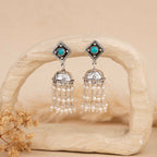 Pair of silver earrings with turquoise stones and pearl-like beads on a beige background