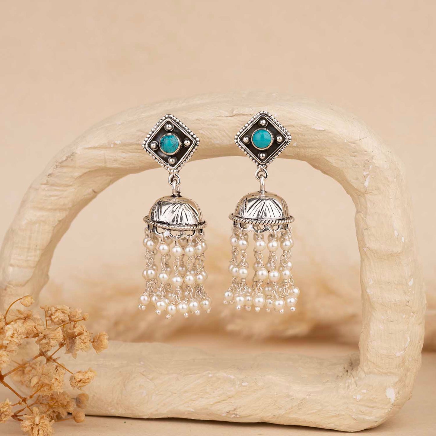 Pair of silver earrings with turquoise stones and pearl-like beads on a beige background