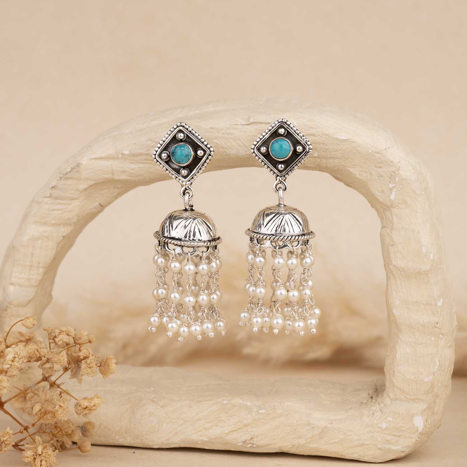 Pair of silver earrings with turquoise stones and pearl-like beads on a beige background