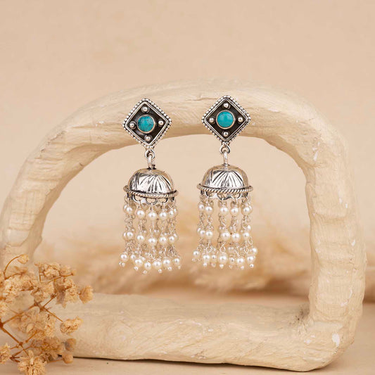 Pair of silver earrings with turquoise stones and pearl-like beads on a beige background