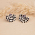 Pair of silver earrings with pearl-like beads and purple gemstones on a beige fur background