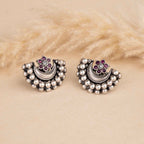 Pair of silver earrings with pearl-like beads and purple gemstones on a beige fur background