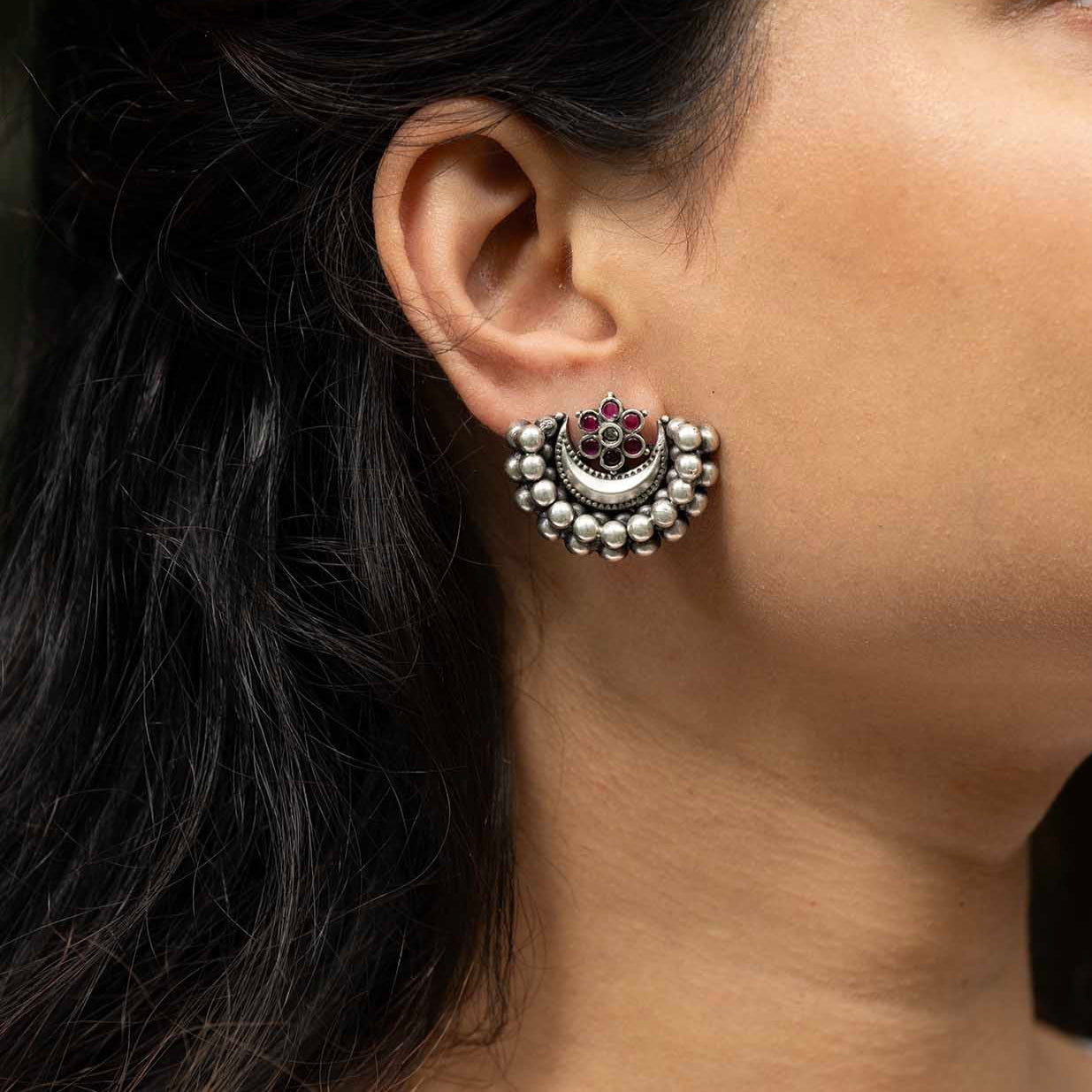 Close-up of an ear wearing a silver earring with a floral design.