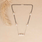 Necklace with black beads and silver pendants on a beige background