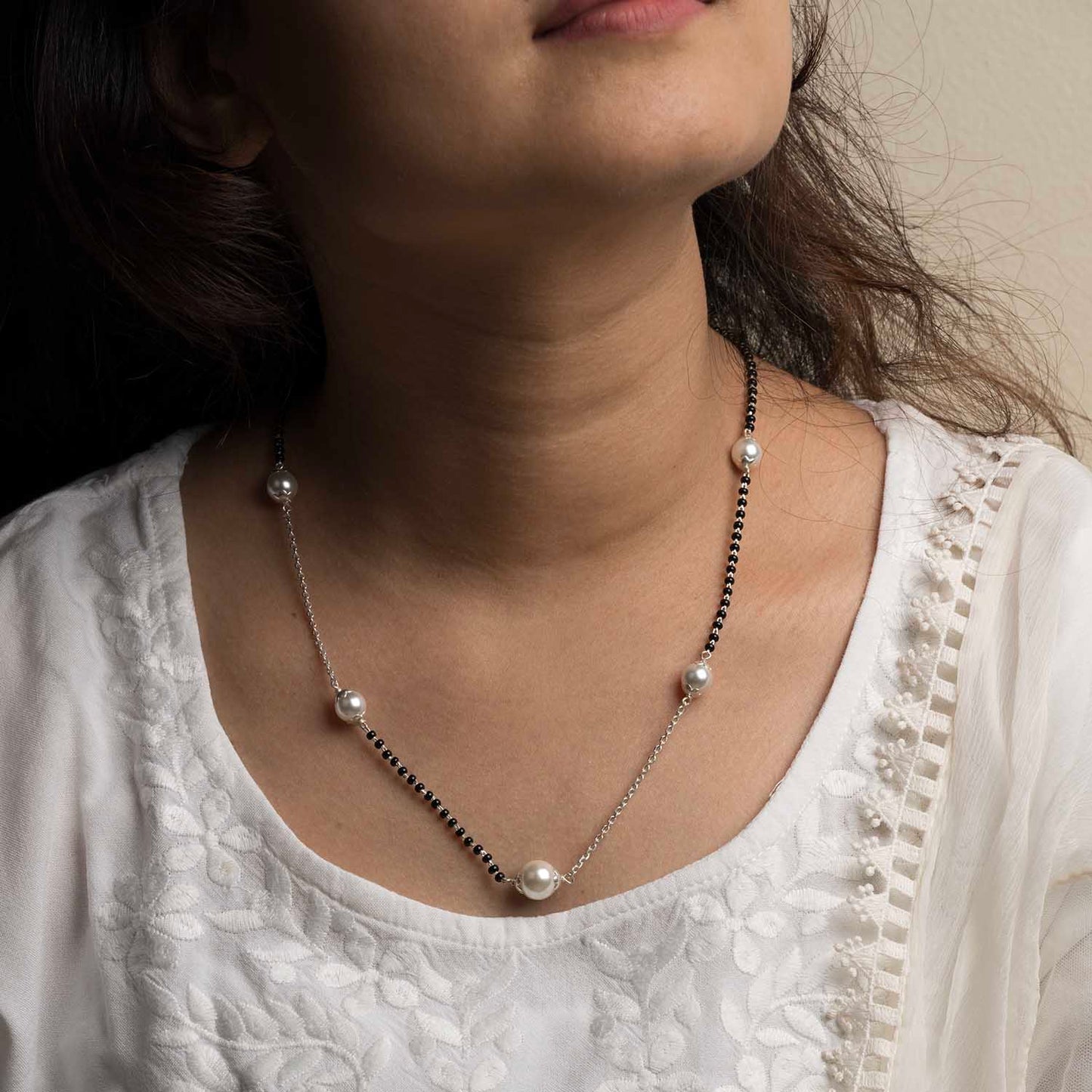 Close-up of a person wearing a pearl necklace with a white top.