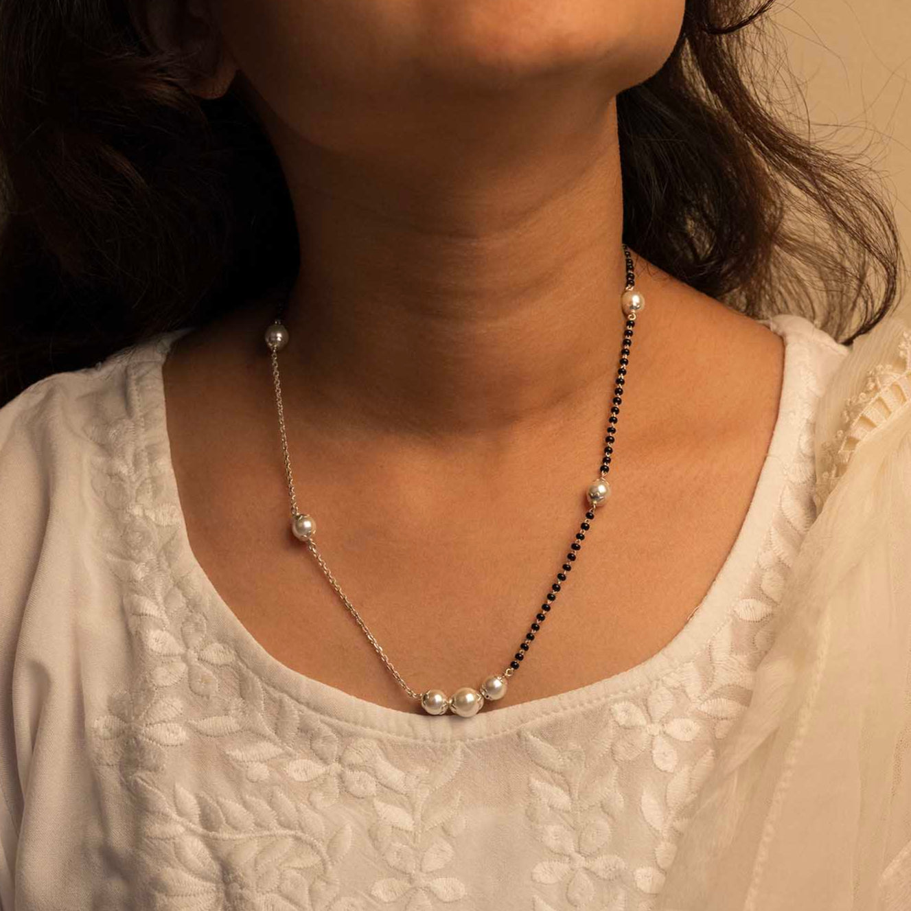 Close-up of a person wearing a delicate necklace with small pearls against a neutral background