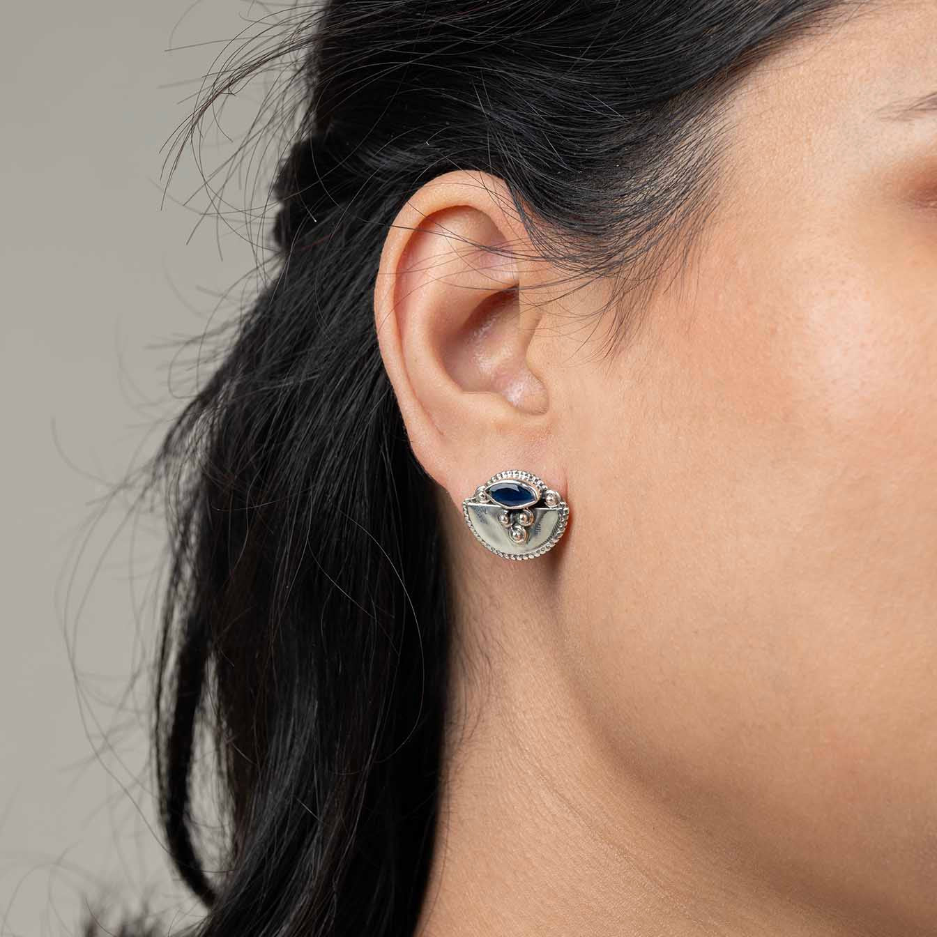 Close-up of a person wearing a silver earring with a blue gemstone on a neutral background