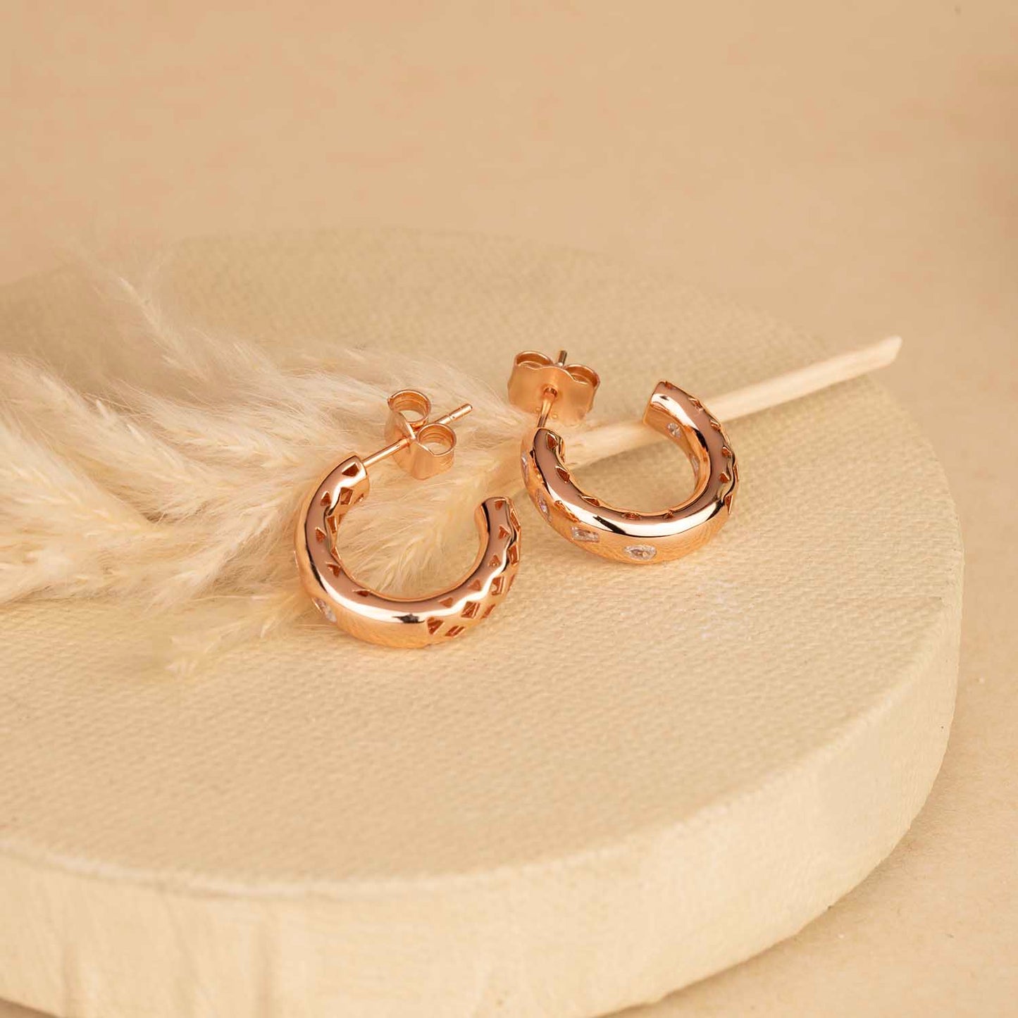 Rose gold hoop earrings on a beige background