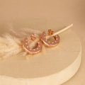 Rose gold hoop earrings with small diamonds on a beige background