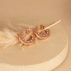 Rose gold hoop earrings with small diamonds on a beige background