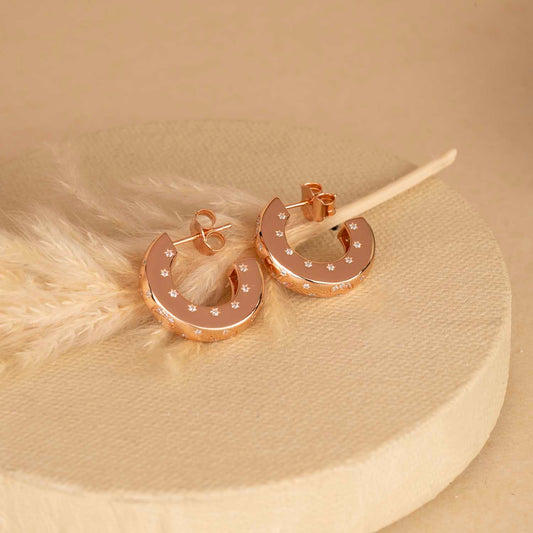 Rose gold hoop earrings with small diamonds on a beige background