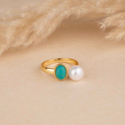 Gold ring with turquoise gemstone and pearl on a beige background