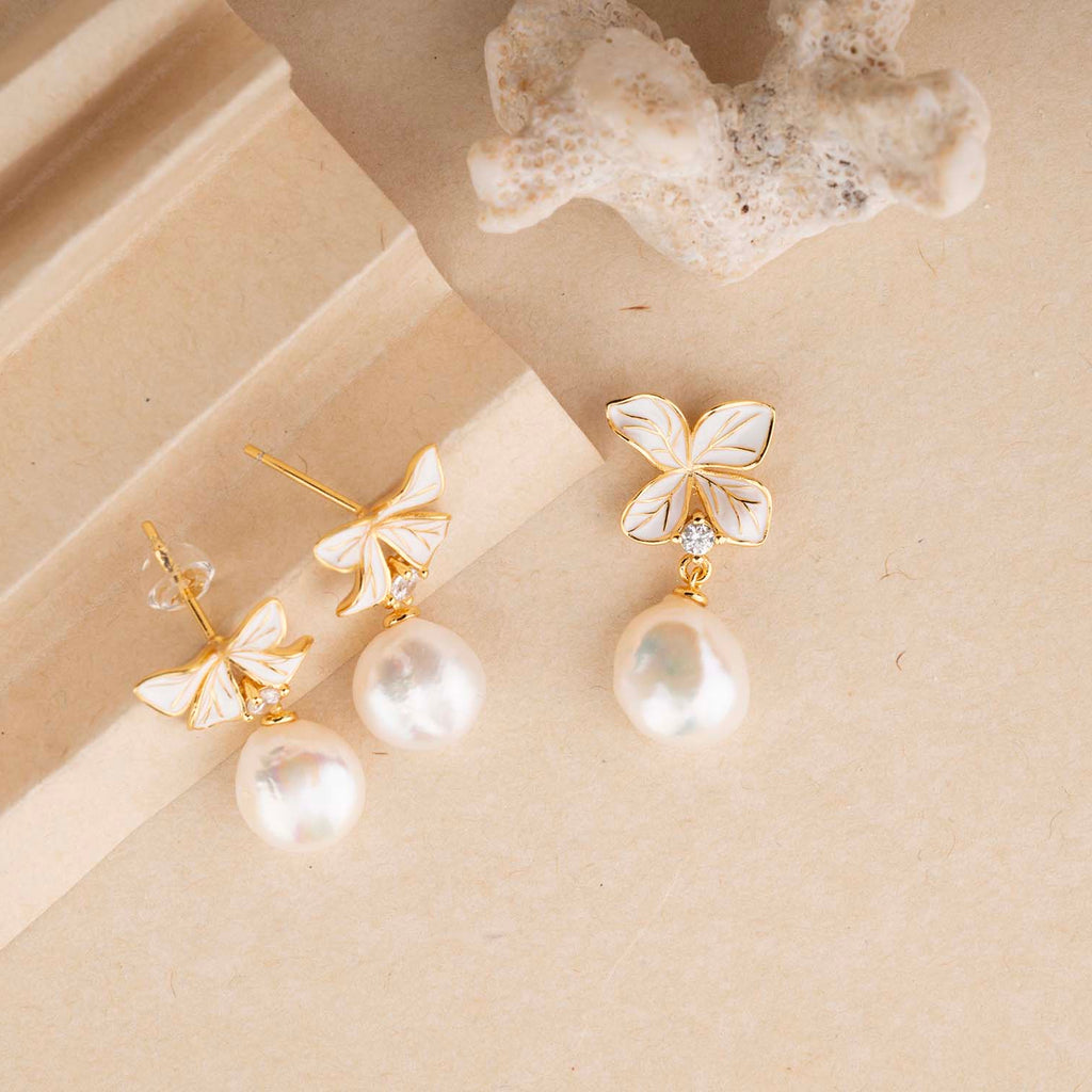 Pair of butterfly-shaped earrings with pearl drops on a beige surface.