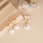 Pair of butterfly-shaped earrings with pearl drops on a beige surface.