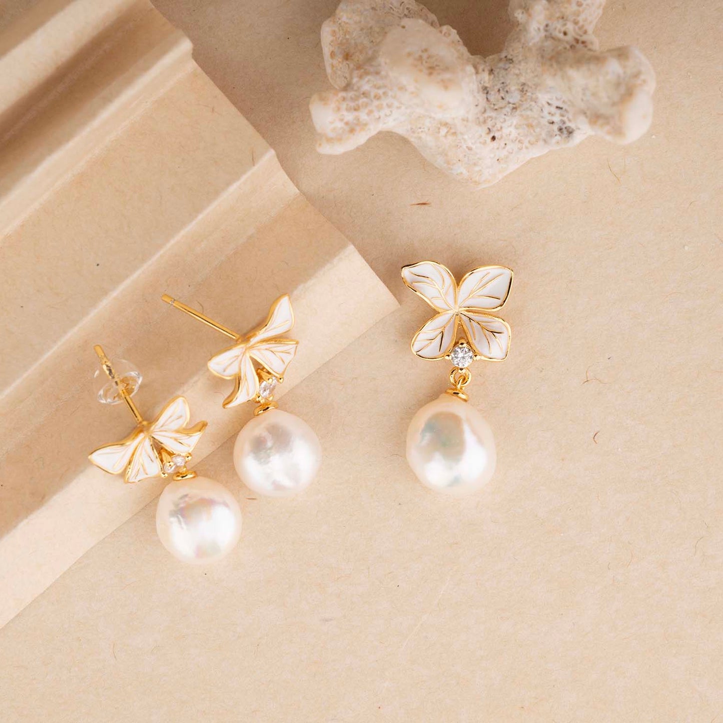 Pair of butterfly-shaped earrings with pearl drops on a beige surface.