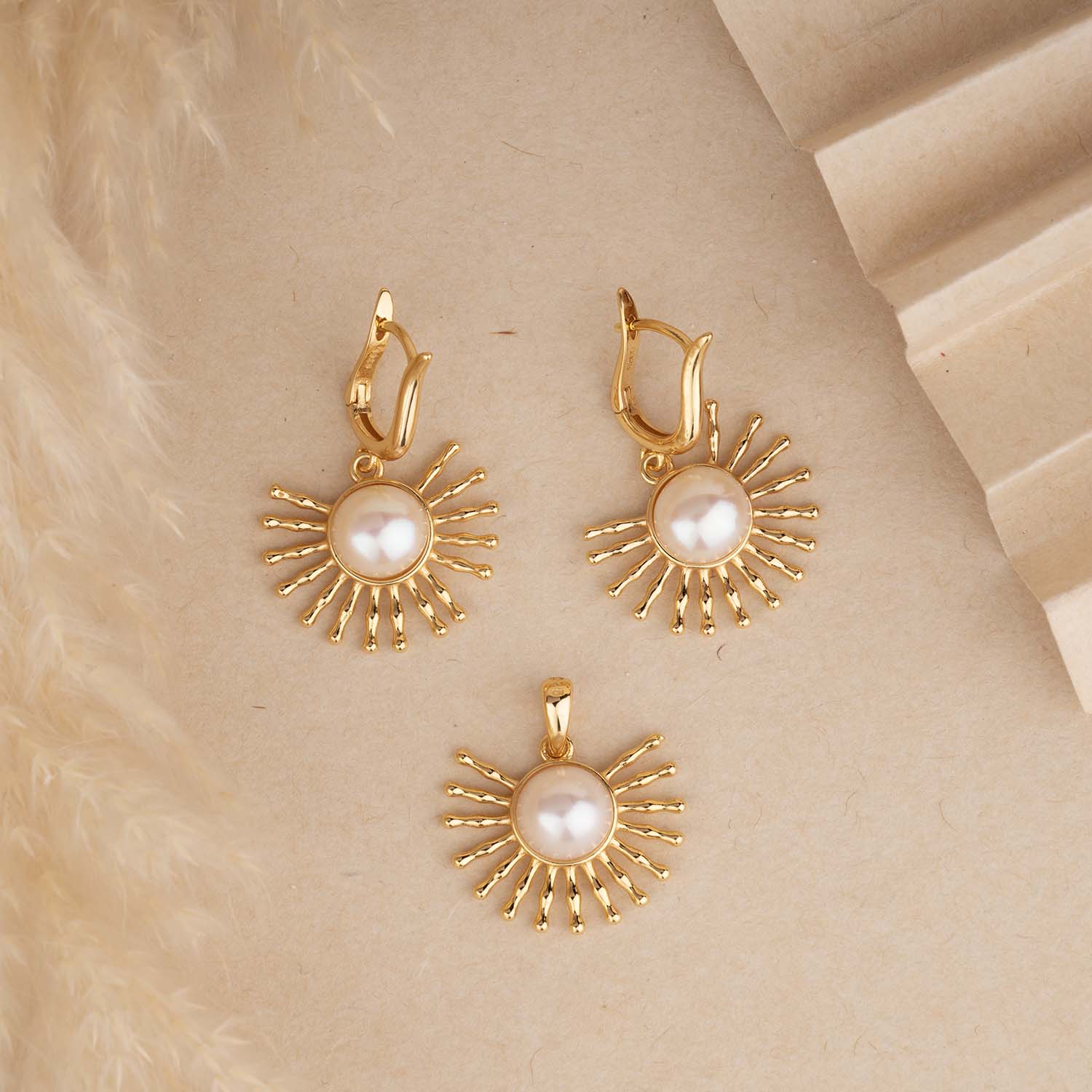 Gold sunburst earrings with pearl centers on a beige surface