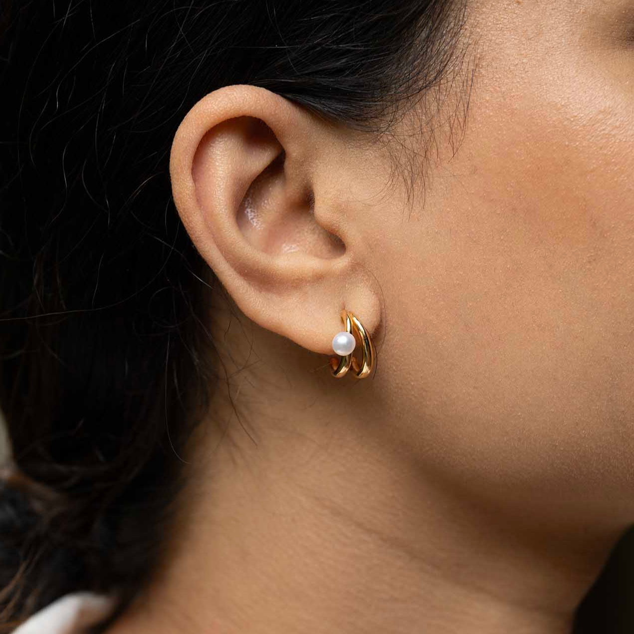 Close-up of a person wearing a gold hoop earring with a pearl accent.
